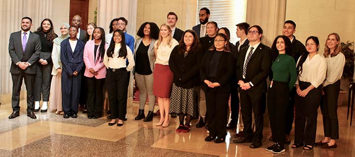 A group of students and their director pose in an ornate hallway.