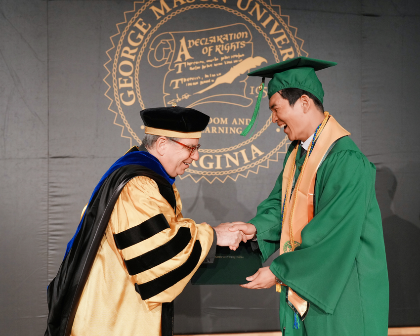 Kim in graduation regalia smiling and shaking hands.