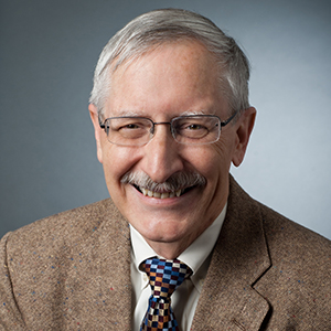 Rich Kauzlarich in a brown blazer and checkered tie and smiling for the camera.