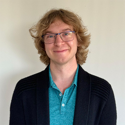 A headshot of CS professor Greg Stein wearing a blue, collared shirt and black sweater.