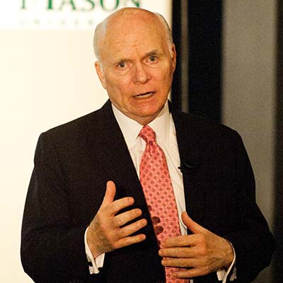 A man in a suit jacket and necktie points toward the camera.