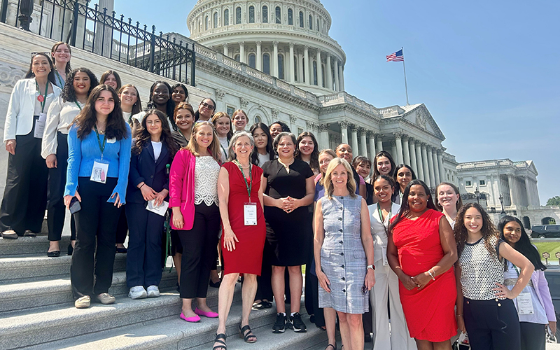A group of women pose for the camera in front of the U.S. Capitol building.