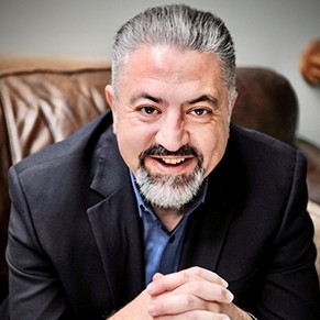 A man in a dark jacket and silver hair smiles at the camera.