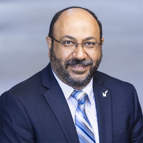 Person wearing a navy suit and blue striped tie against a neutral background