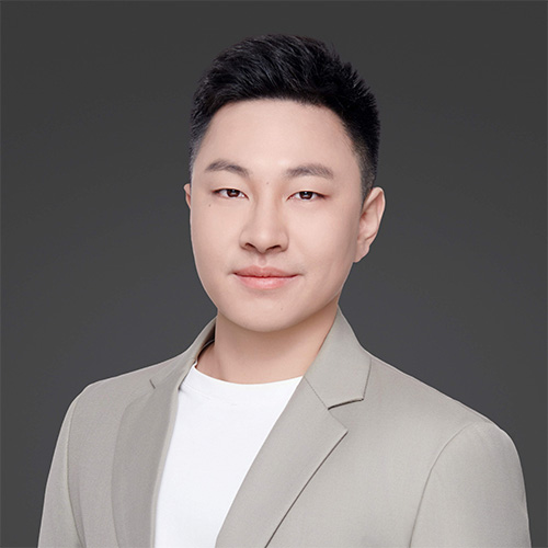Person in a beige blazer and white T‑shirt against a dark gray background