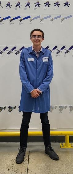 George Mason student Michael Riggi stands holding his hands in front of him while wearing a long blue Northrop Grumman shirt at his internship.