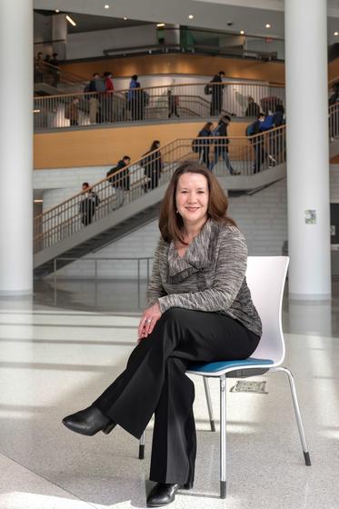 Portrait of Rachel Wernicke in Horizon Hall, with students climbing the stairs behind her