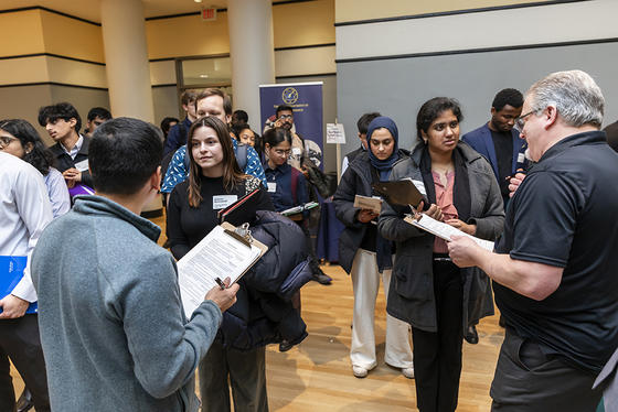 Students in business professional attire line up to speak with company representatives.