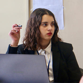 A woman with dark hair holds a pen and looks off camera.