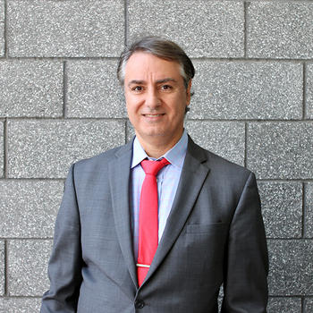 A man in a grey suit and red tie gazes at the camera.